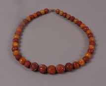 A necklace of carved copal resine beads, graduated circular outline with base metal screw