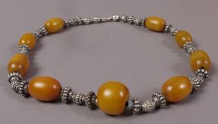 An amber and composite necklace, the nine graduated oval beads separated by ribbed and faceted