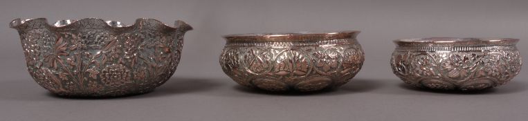Three Indian white metal on copper bowls, all-over worked with plants forms, 9.25cm x 10.5cm x