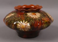 A Linthorpe pottery squat circular vase, c.1885, with wavy rim, decorated with daisies on a brown