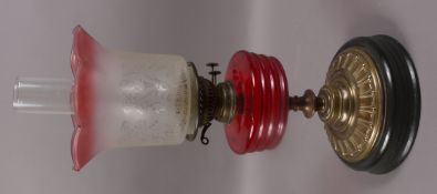 An oil lamp with ruby glass reservoir and etched shade on a brass and metal base