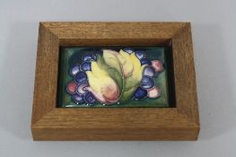 A FRAMED MOORCROFT POTTERY LID, leaf and berries design, impressed and painted marks to base, length