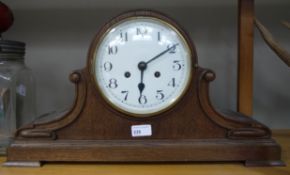 An oak cased mantel clock of arched outline the white enamel circular dial with black Arabic