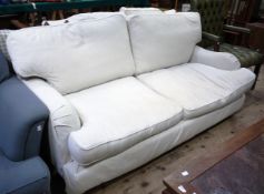 A modern three seater sofa upholstered in oatmeal fabric on turned legs with brass caps and castors