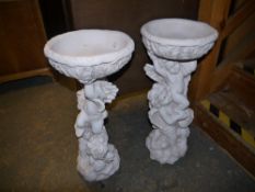 A pair of bird baths with cherub columns